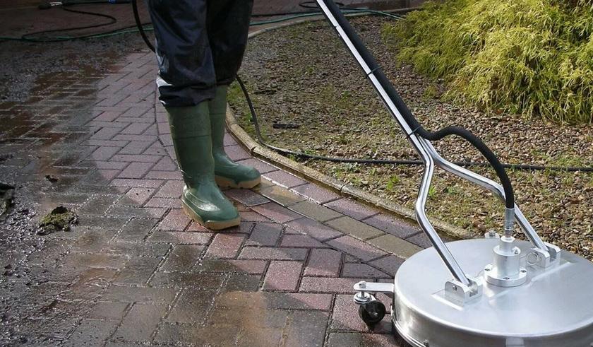 Rotary surface cleaner lifting grime from a paved driveway